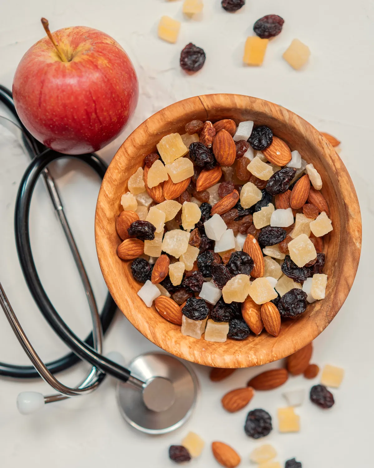 A stethoscope beside a bowl of almonds and dried fruit and a red apple